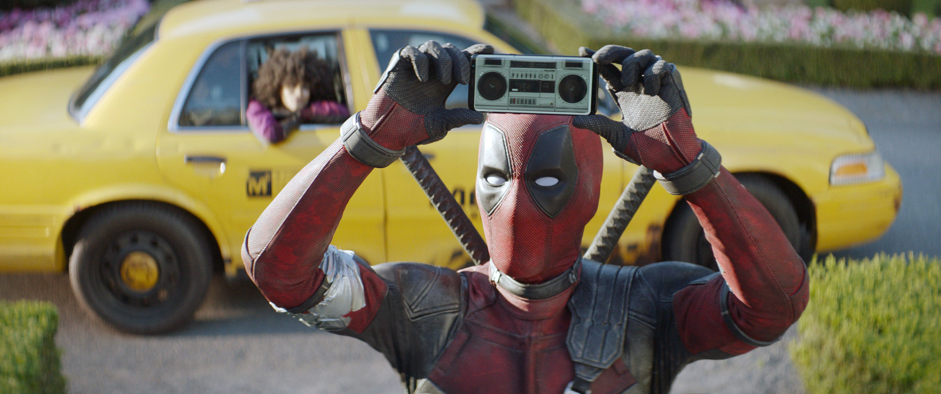 deadpool holding up a small tape deck playing music while a cab waits behind
