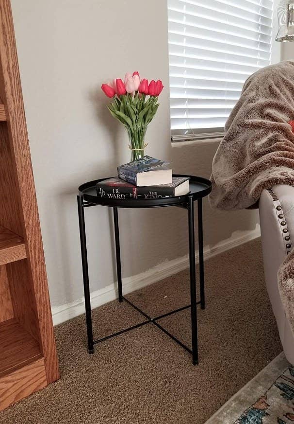 A black, metal side table with a round removable tray atop