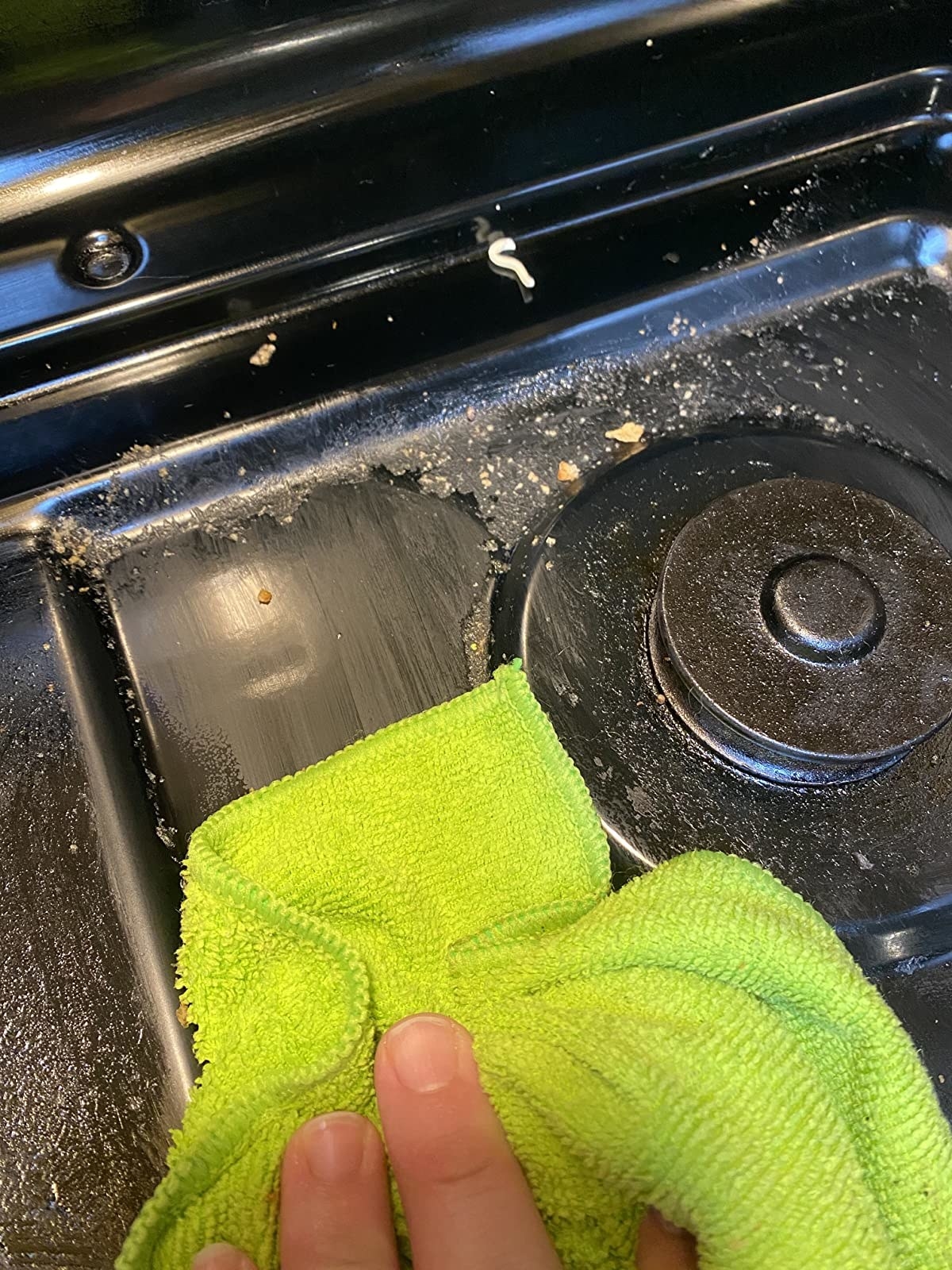 close up of reviewer using a lime green microfiber cloth to remove grease from a stovetop