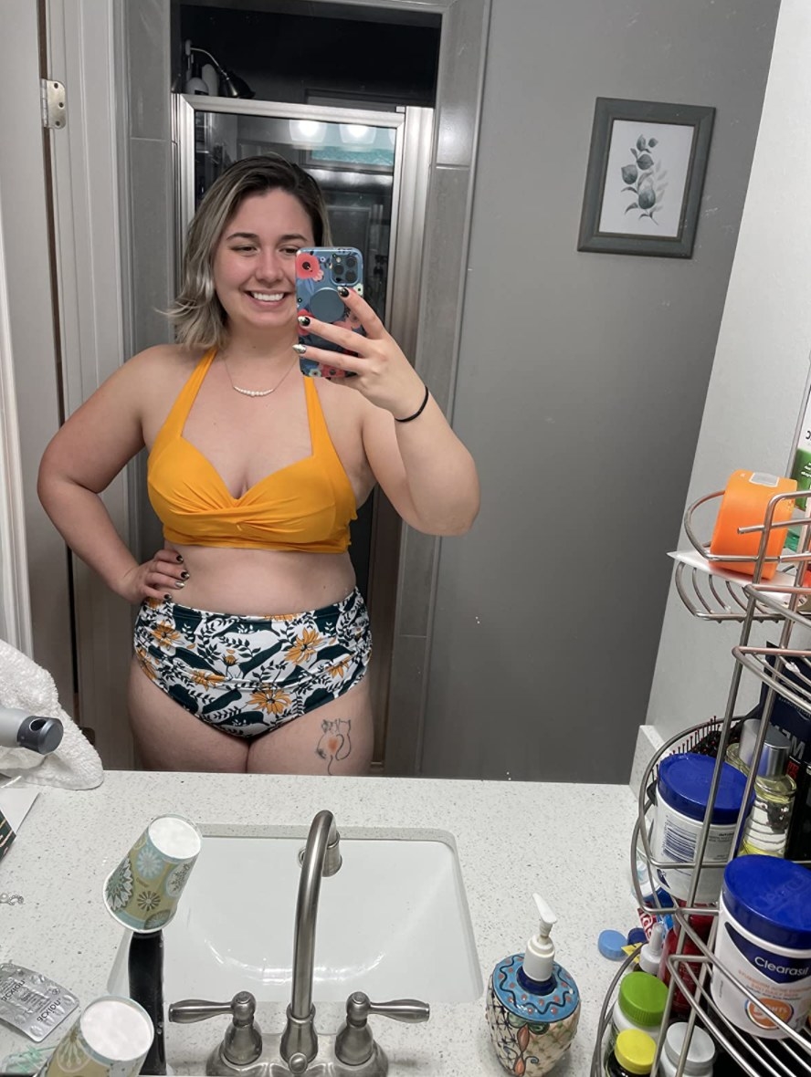 reviewer wearing the suit with a yellow top and floral bottoms
