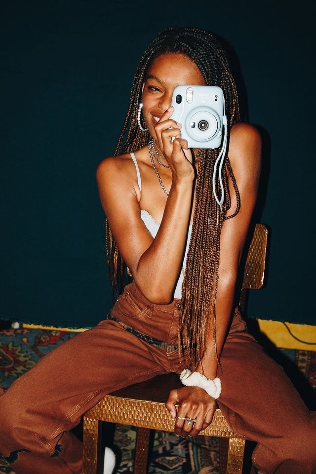 model holds light blue Fujifilm Instant Camera in their hands to snap a photo
