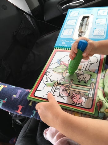 Reviewer's photo showing their child coloring with a water pen on the pad in a car