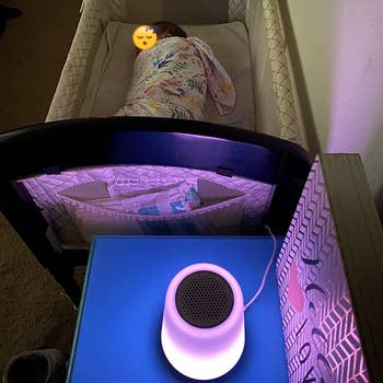 The night light emanating a purple light on the side table near the baby sleeping in a crib