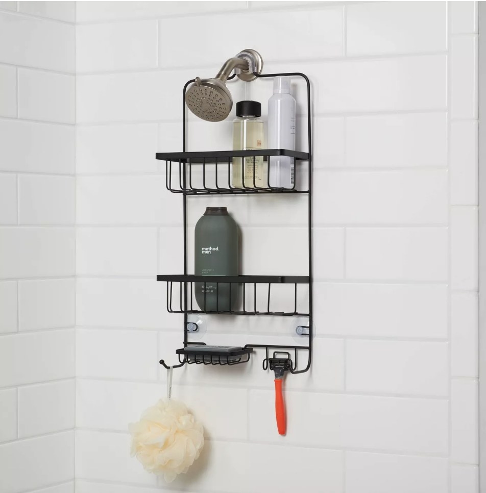 The black shower caddy against white tile with razor, sponge, and bottles inside