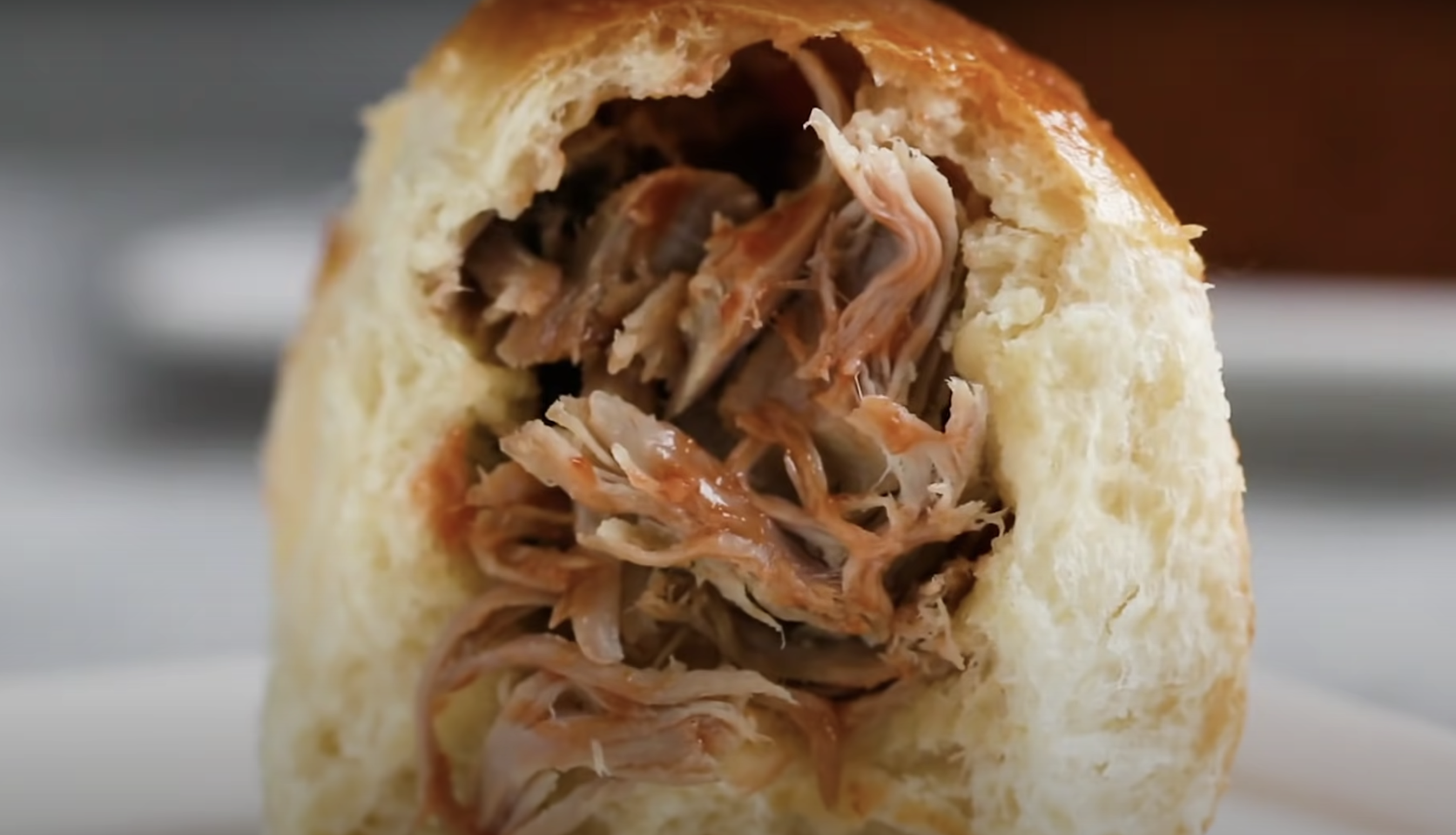 A milk bun pulled in half showing the pulled pork filling.