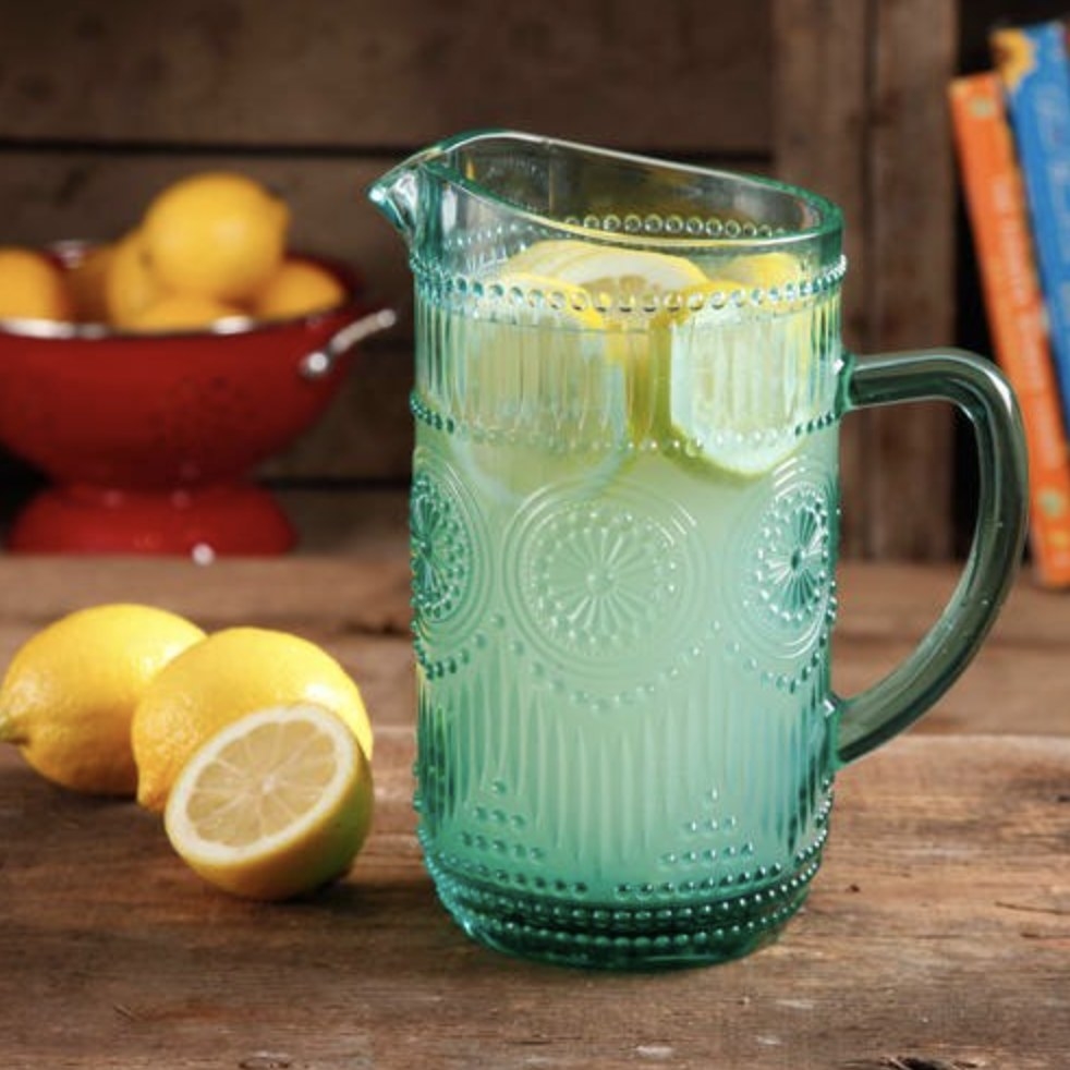 The turquoise glass pitcher is holding lemonade and slices of lemonade