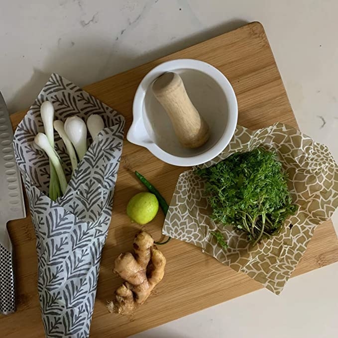 Green onions and some green wrapped in beeswax wrap on a chopping board