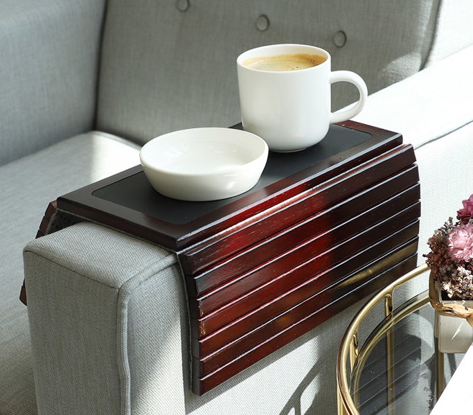 The tray with a coffee mug and bowl on it resting on the arm of a chair