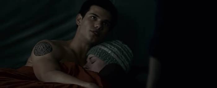 Jacob, Edward, and Bella are sitting together in a tent while Jacob warms Bella's body