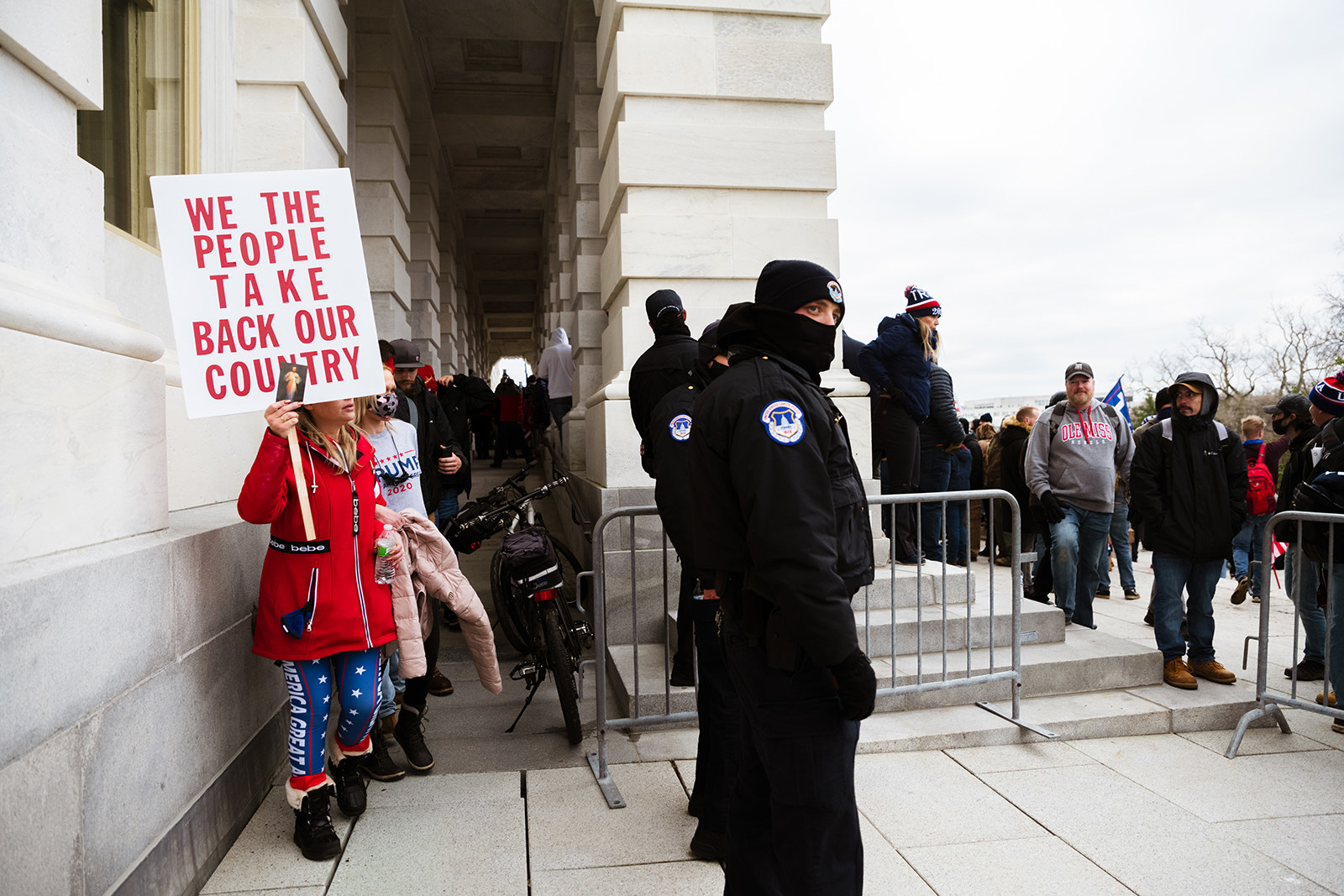 A woman in Trump-themed leggings holds a sign reading &quot;we the people take back our country&quot; near police