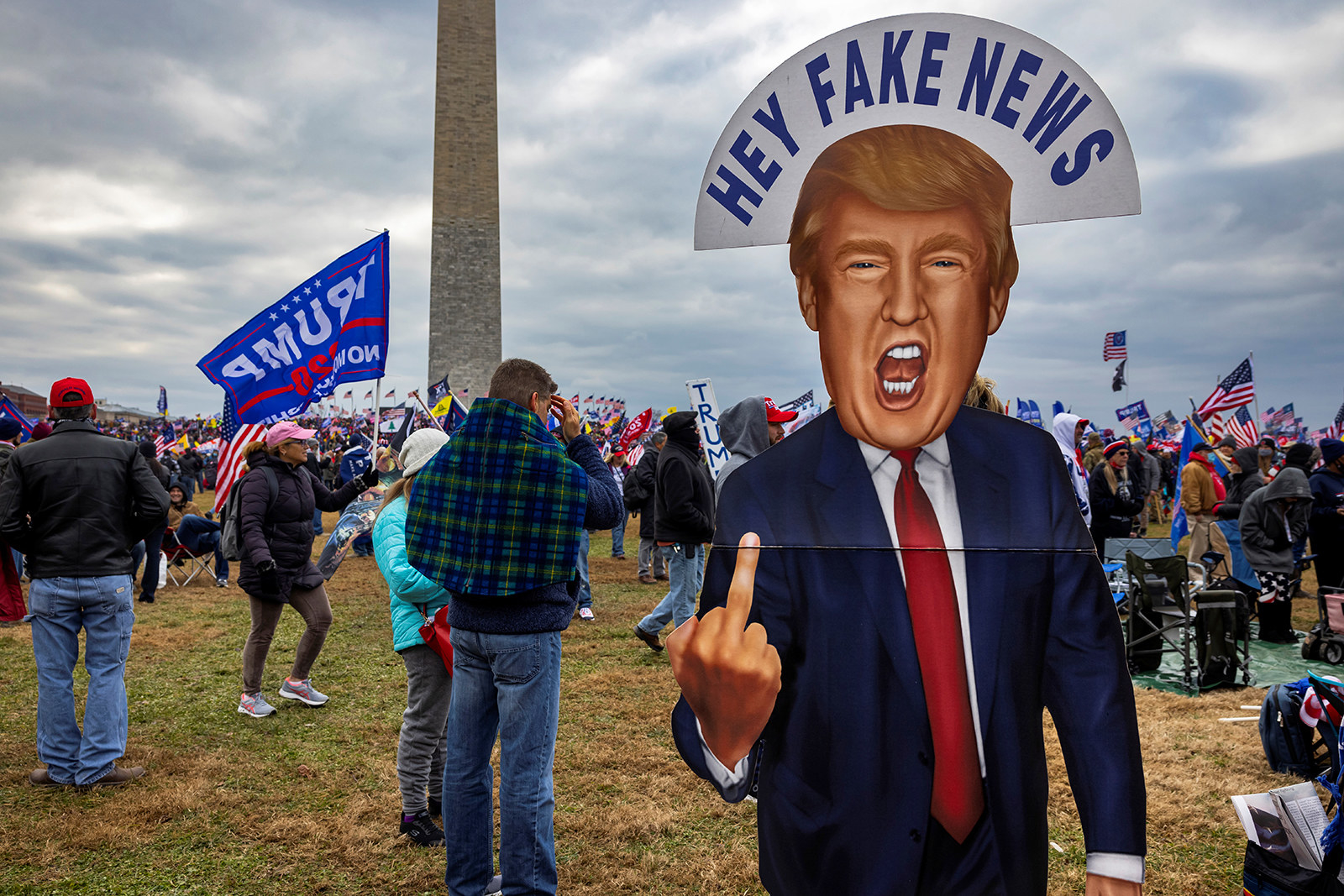 People stand near a cardboard cutout of Trump with a sign reading &quot;Hey Fake News&quot; over his head as he flips off the camera 