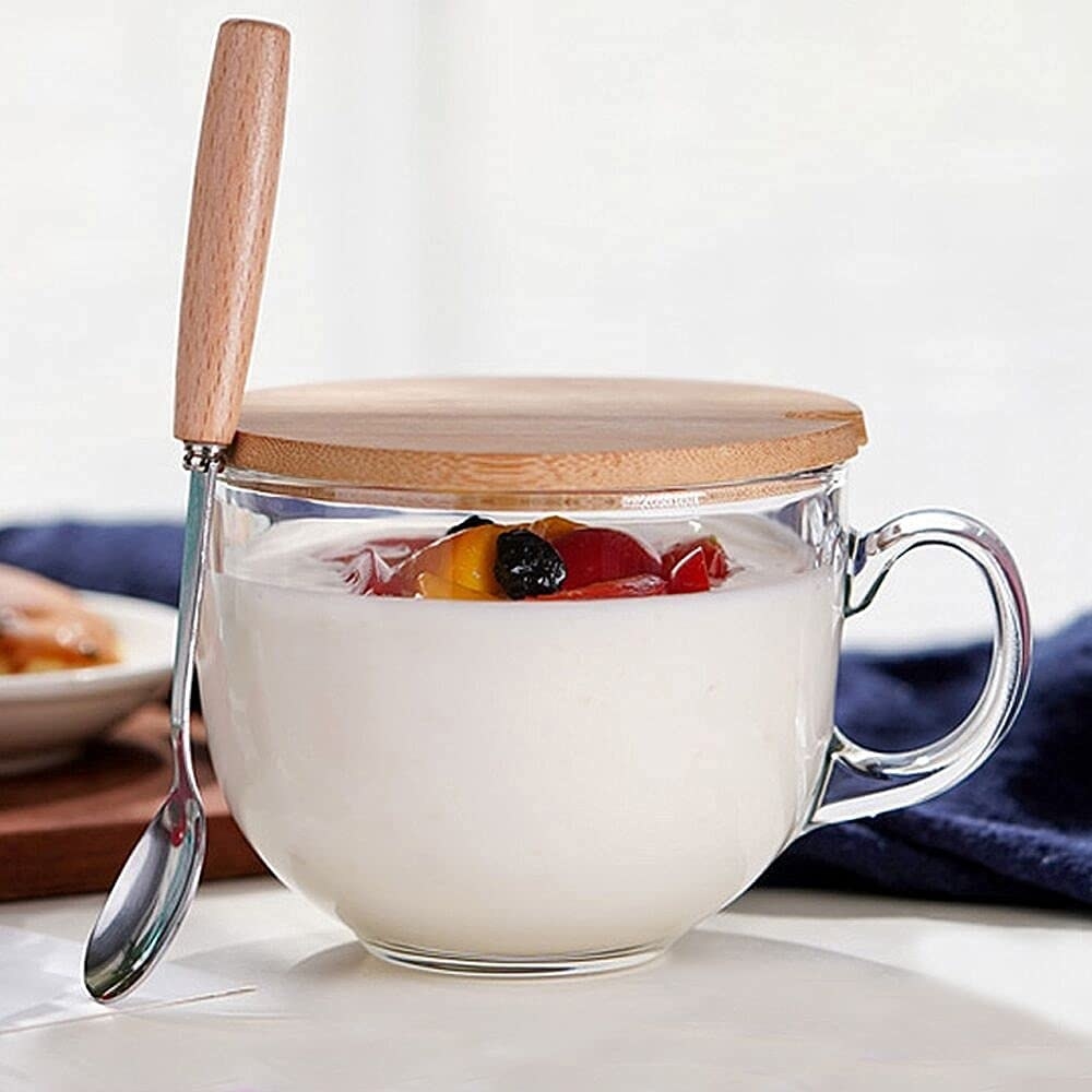 A dessert-filled mug covered with a bamboo lid and a spoon attached to it