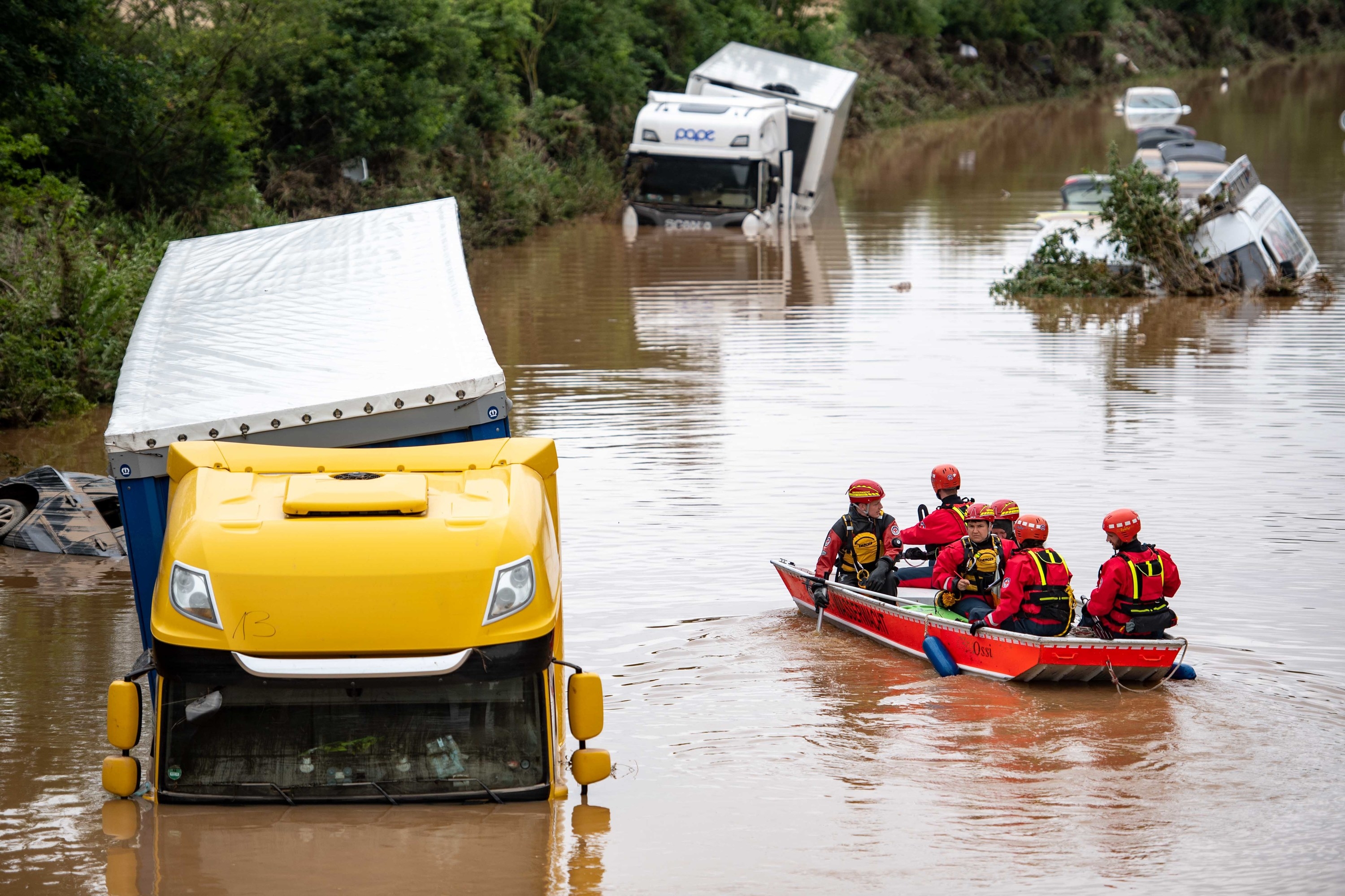 submerged trucks on a highway are approached by firefighters in a boat