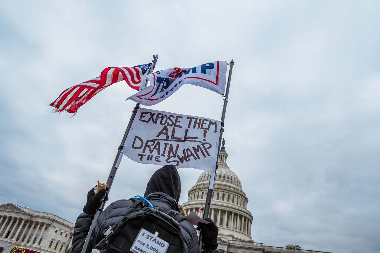 A man holds a sign reading &quot;Expose them all drain the swamp&quot; 