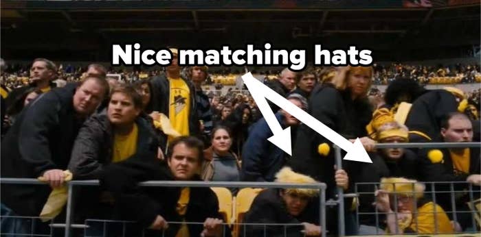 Crowd looking frightened, and a couple wearing silly yellow and black hats hiding behind a rail
