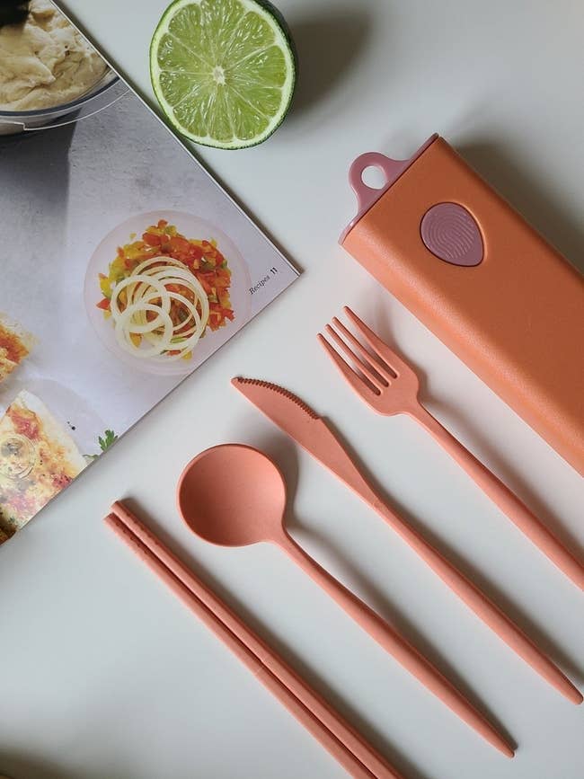 pink chopsticks, spoon, fork, and knife with pink case next to book
