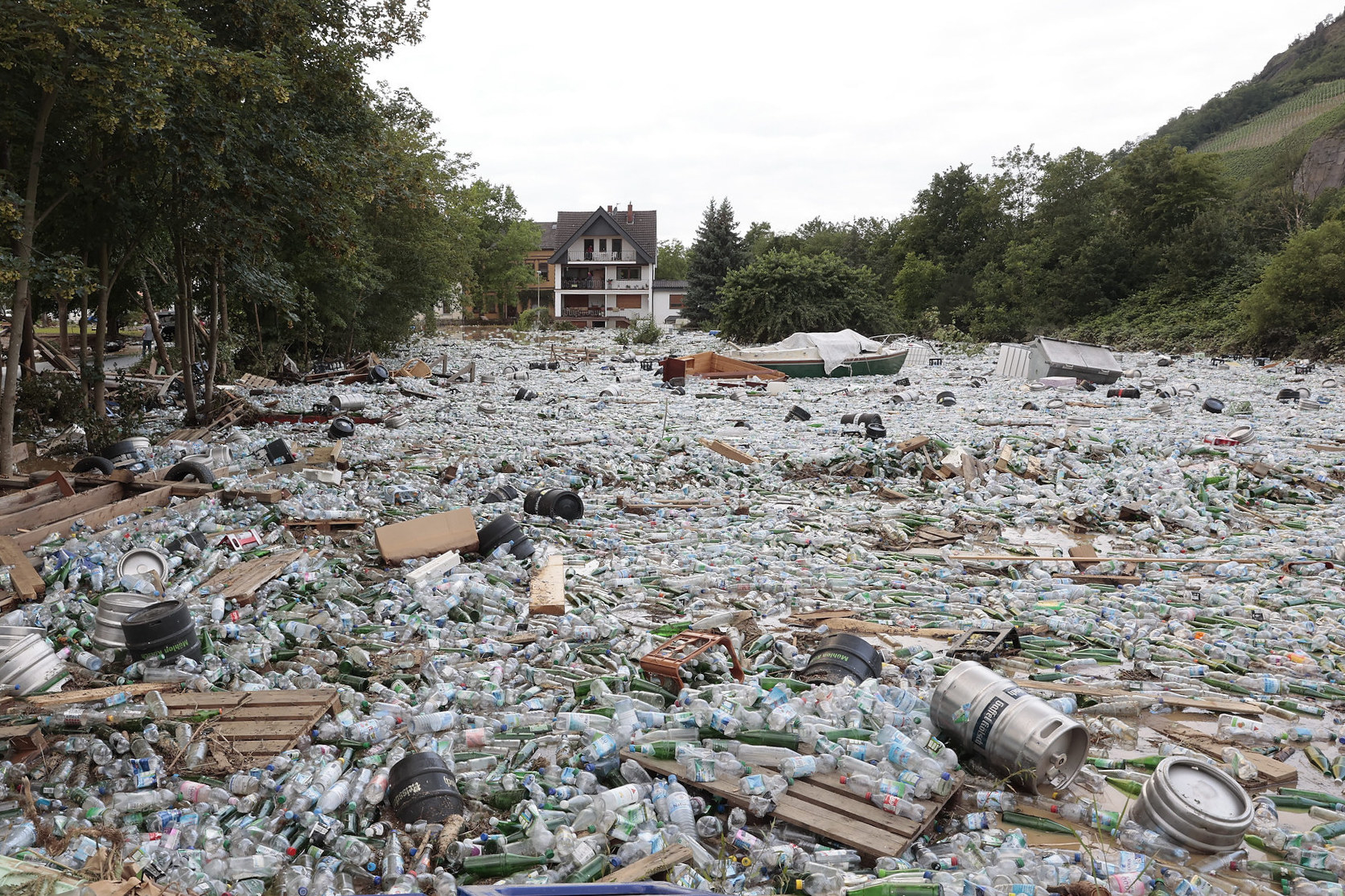 A large area of ground is covered in plastic water bottles, glass bottles, and beer kegs