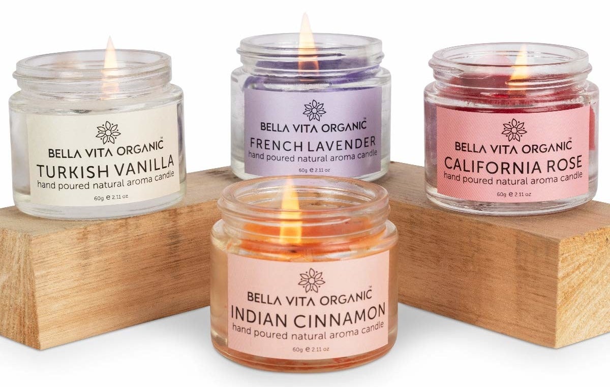 Four scented candles laid around a wooden block in Turkish Vanilla, French Lavender, California Rose, and Indian Cinnamon scents