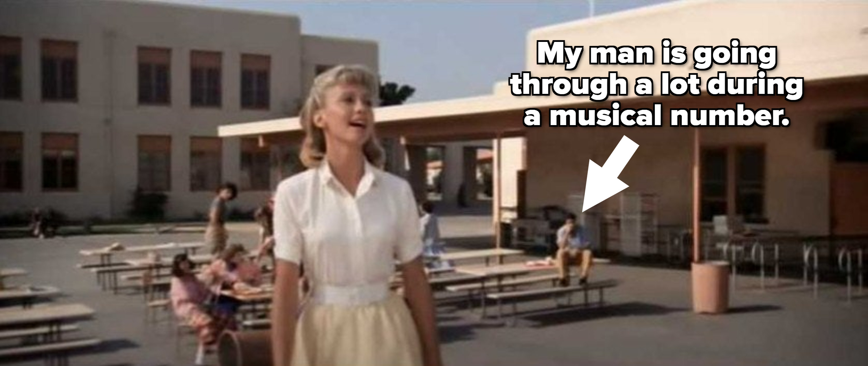 Sandy from &quot;Grease&quot; singing while a man sits in the background on the table in deep thought