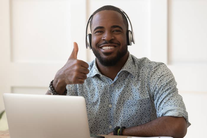 Man motions a thumbs-up beside his laptop