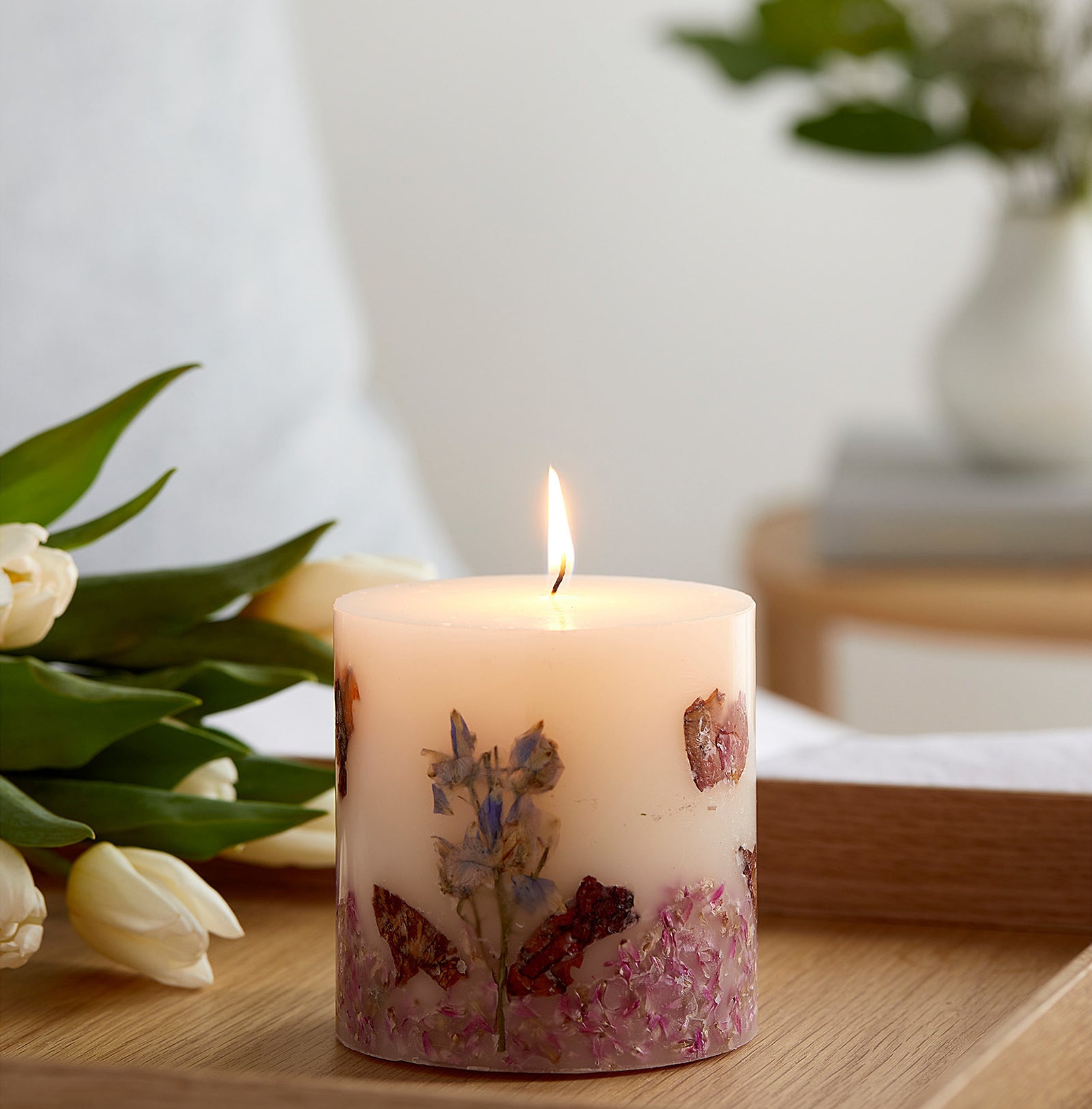 a lit candle on a tray next to a bouquet of tulips