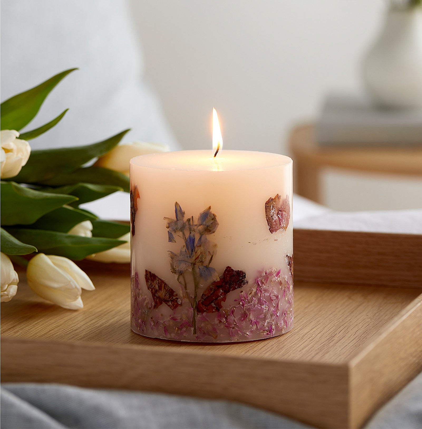 a lit candle on a tray next to a bouquet of tulips