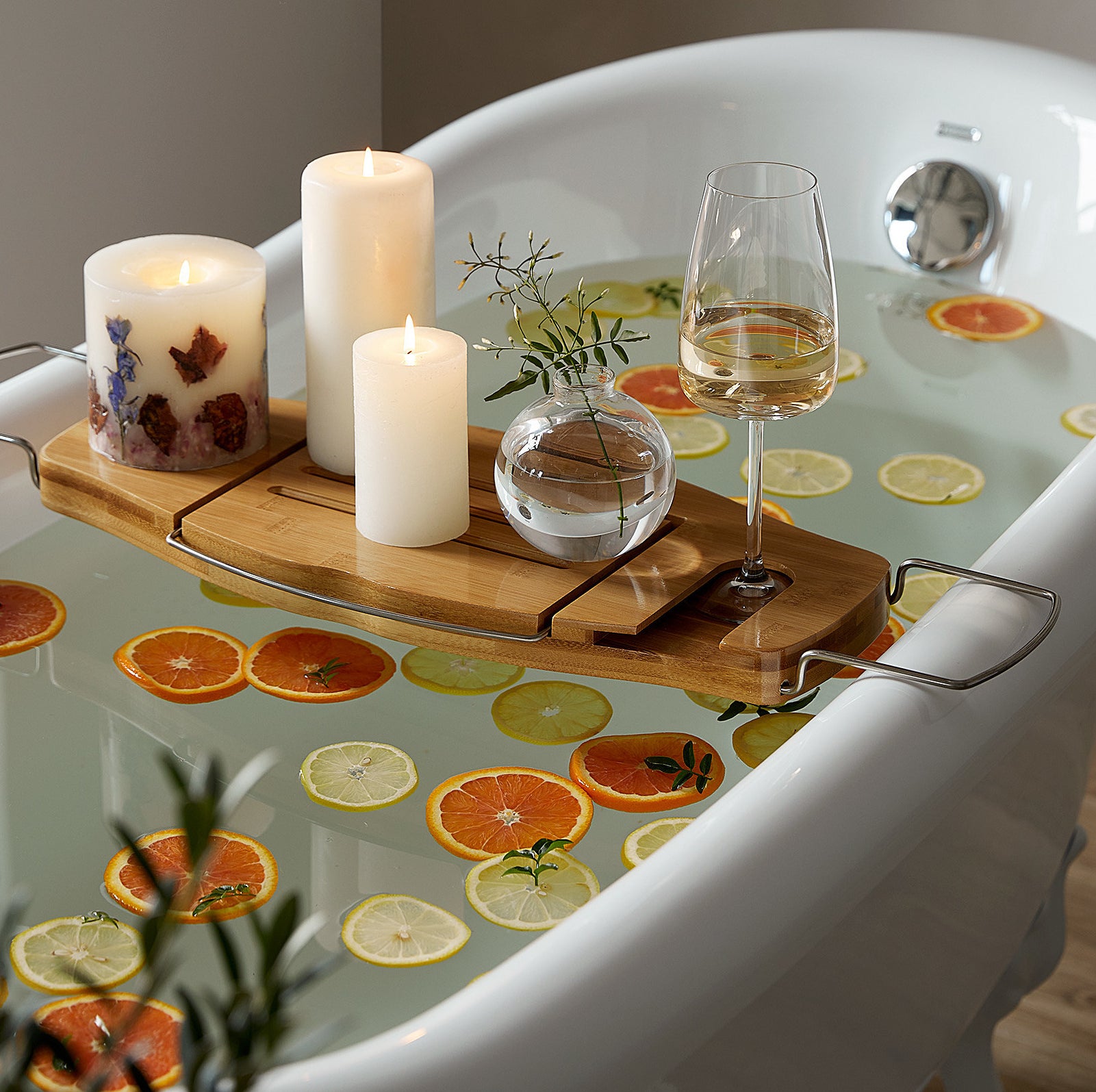 a tub filled with citrus slices with the tub tray on top holding candles and wine