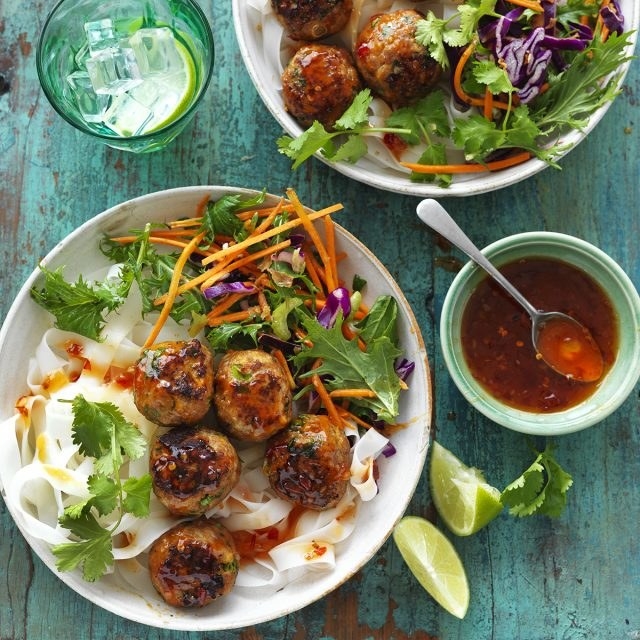 Five curry meatballs on a bed of rice noodles with coriander and carrot and lettuce garnish.