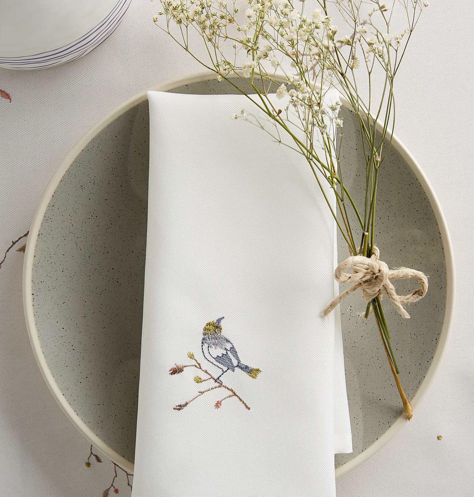 a napkin with a bird embroidered on it on a plate on a table