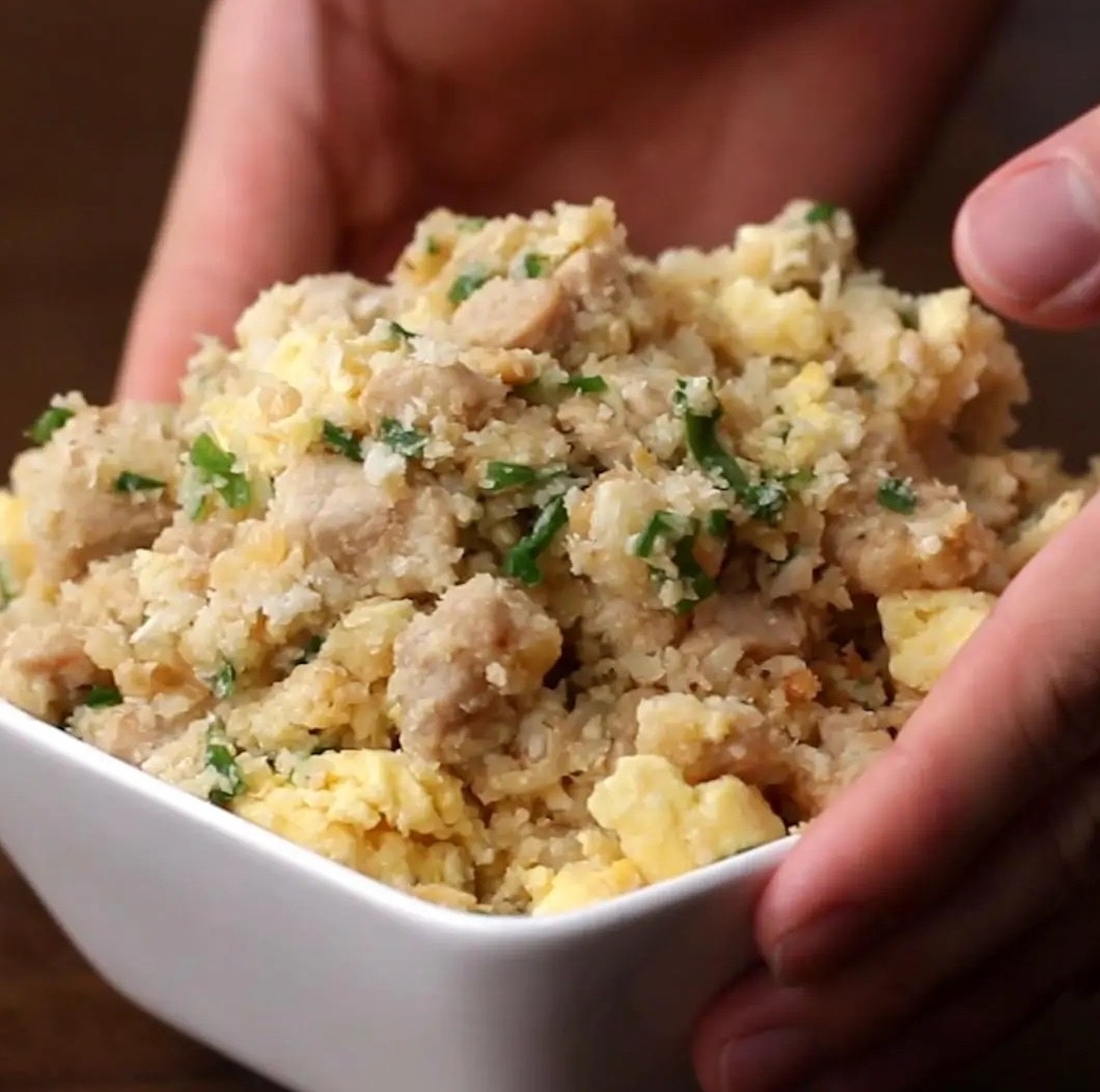 A pair of hands holds a bowl of garlic pork and cauliflower rice