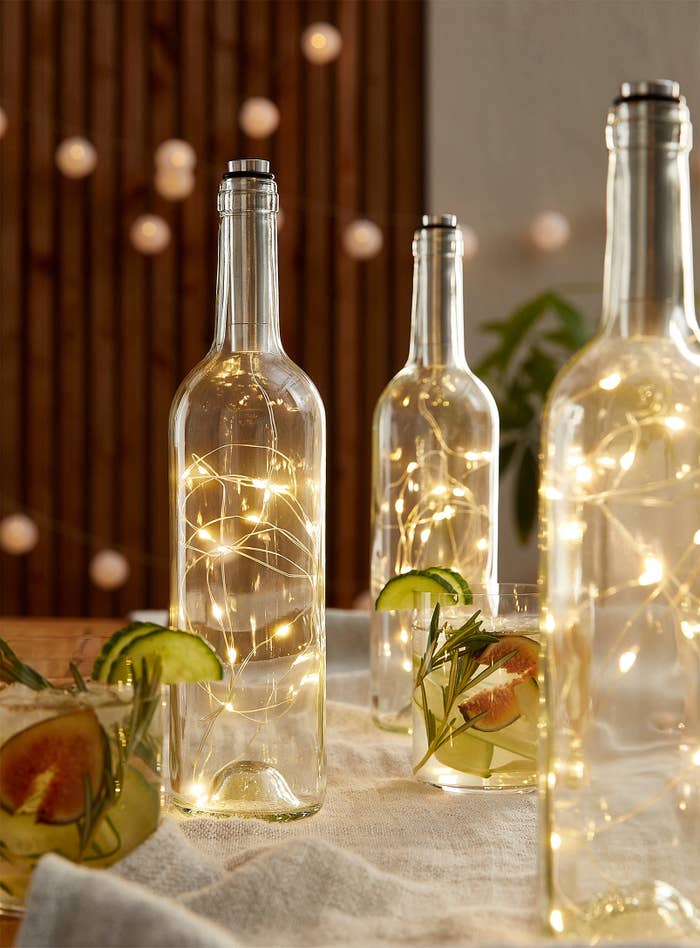 the bottles with fairy lights in them on a table next to cocktails