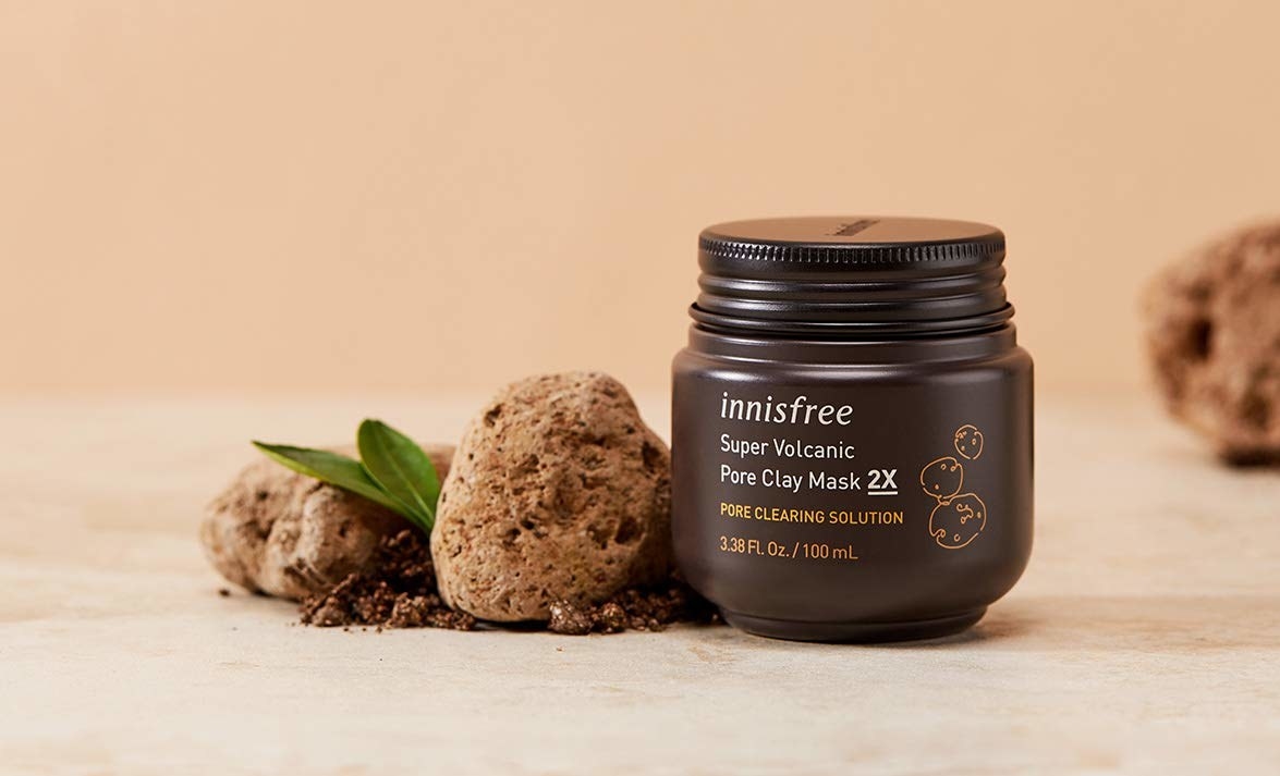 A tub of Innisfree Super volcanic clay mask with earth and volcanic clay particles spread around it.