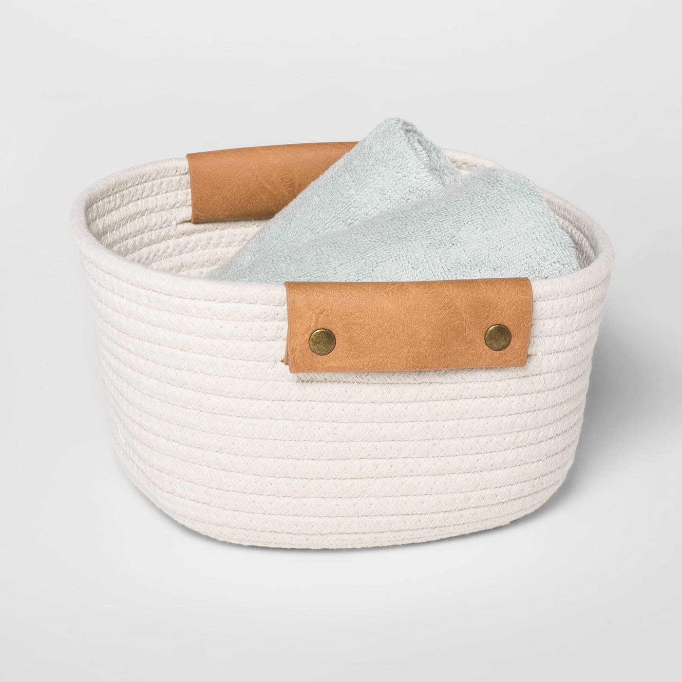 A white coiled rope storage basket with towels in it