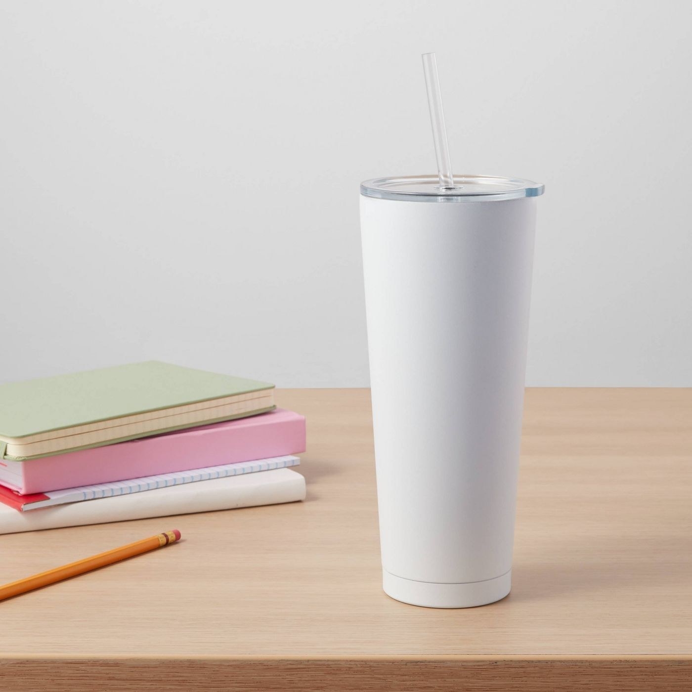 A white stainless steel tumbler with a lid and straw on a desk