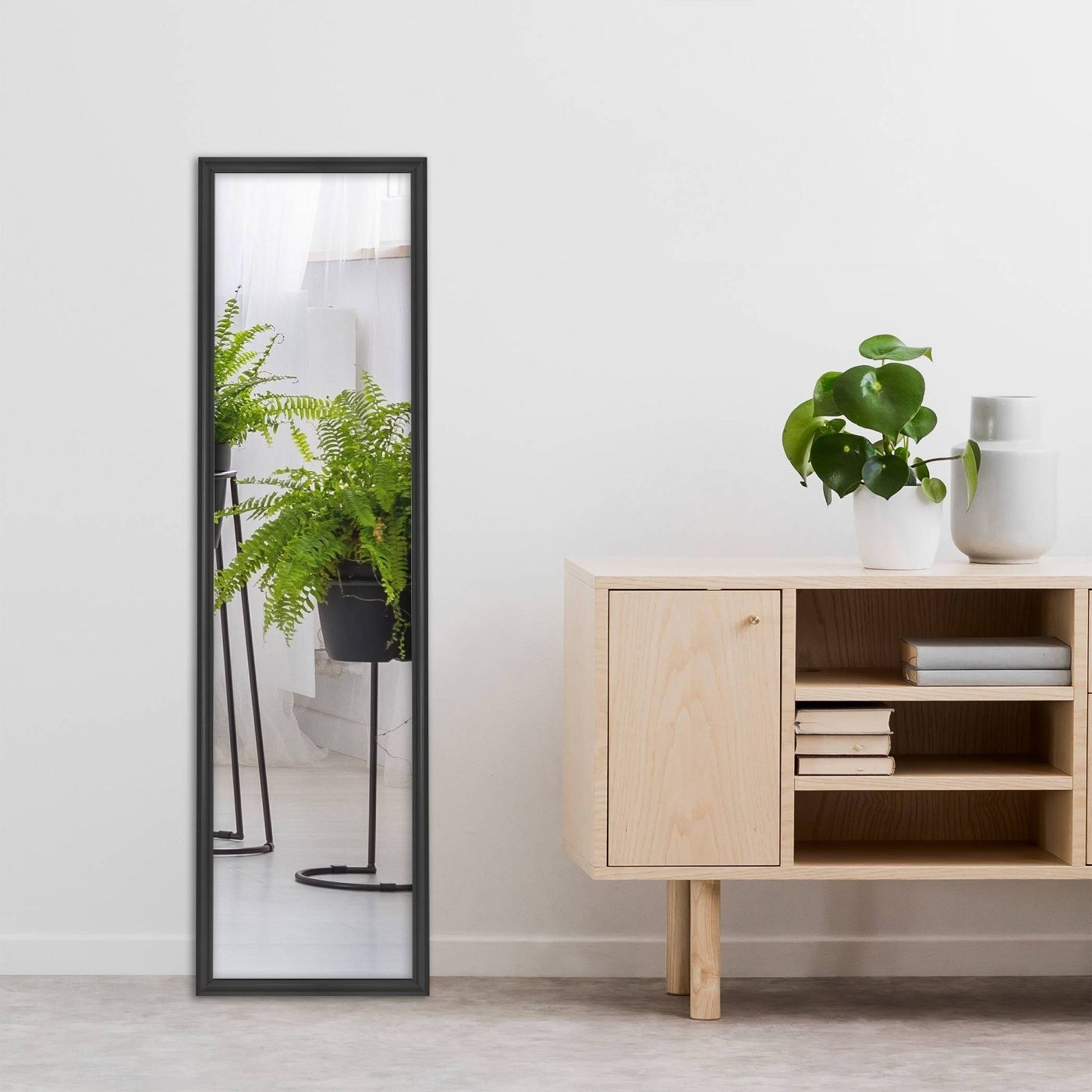 A blacked framed full length mirror leaning against a wall next to a console table