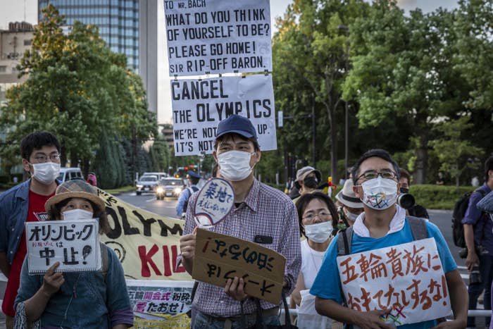 People wearing masks and signs in Japanese and English (&quot;Cancel the Olympics&quot;)