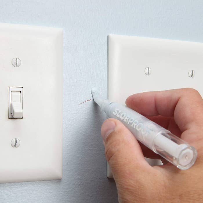 A person using the pen to cover up a scratch between light switches