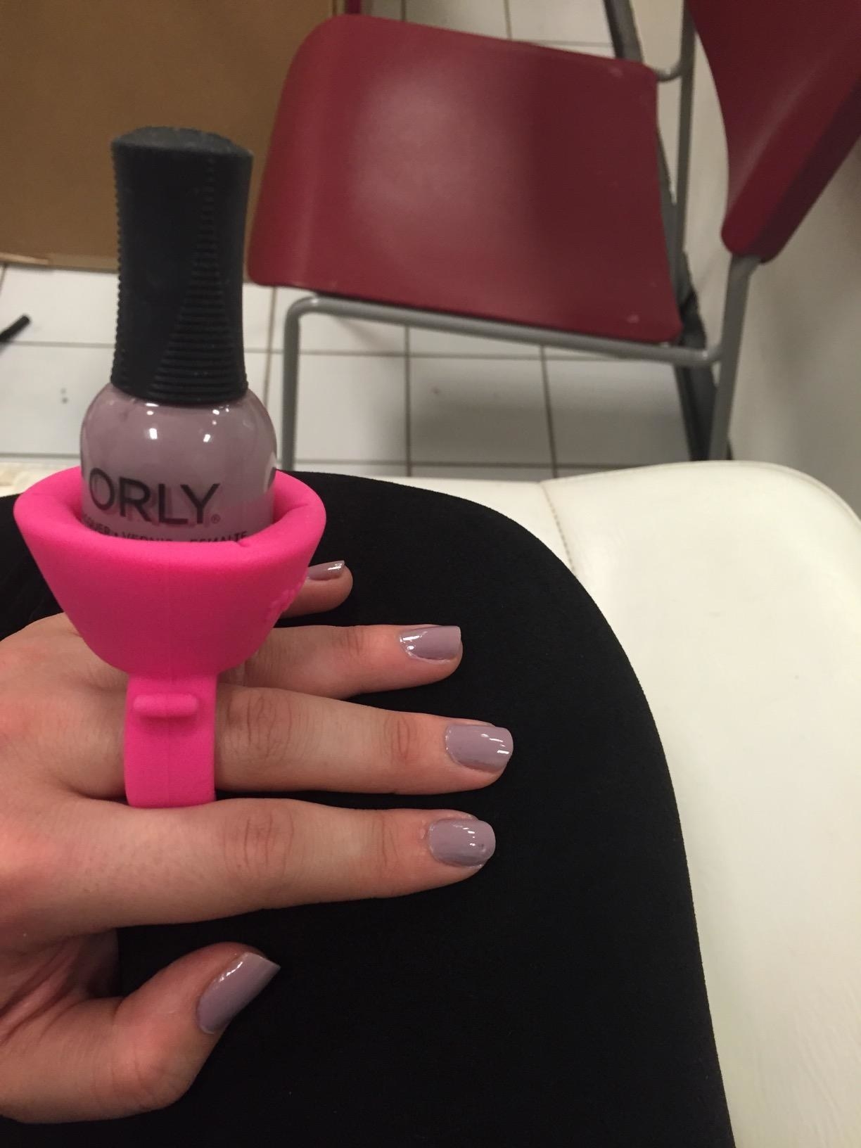 reviewer painting their nails while using the nail polish bottle holder, which is securely on their fingers