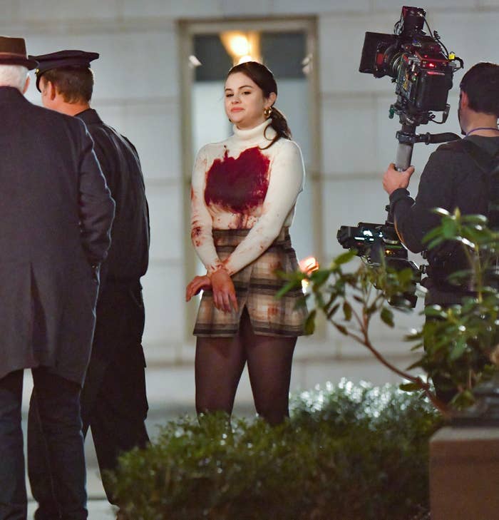 Selena filming a scene while wearing a blood-stained turtleneck and a plaid skirt