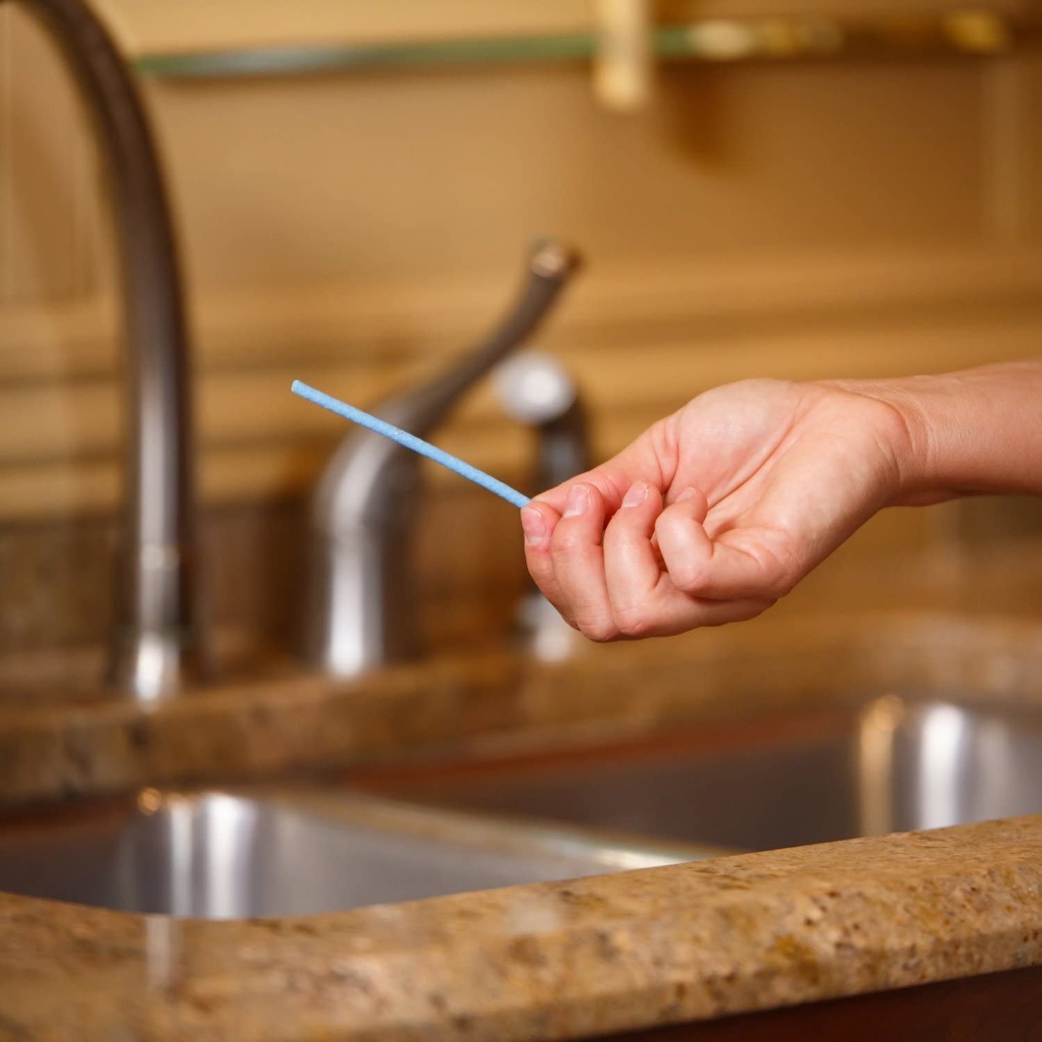 A person holding one of the sticks in front of a sink