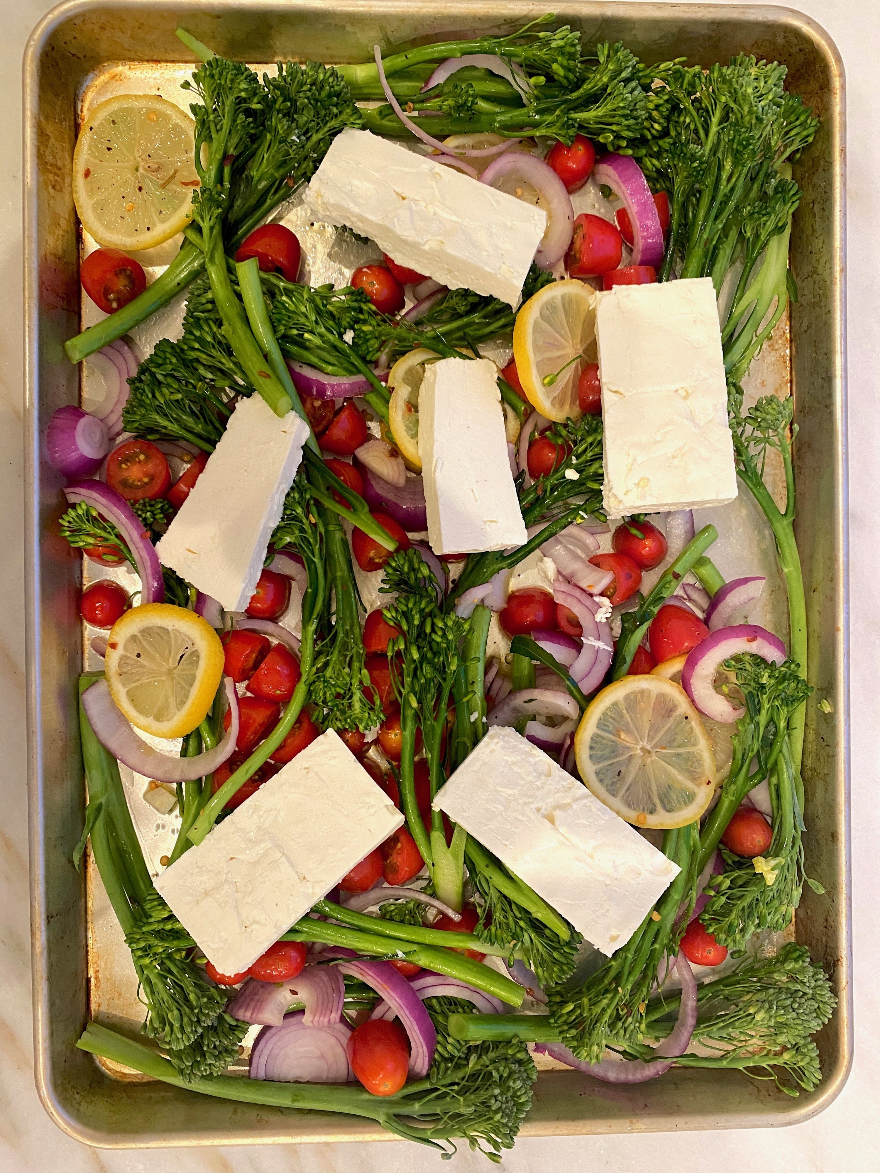 Vegetables on a sheet pan with blocks of feta