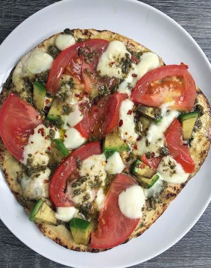 A naan pizza with tomatoes, avocado, mozzarella, and pesto