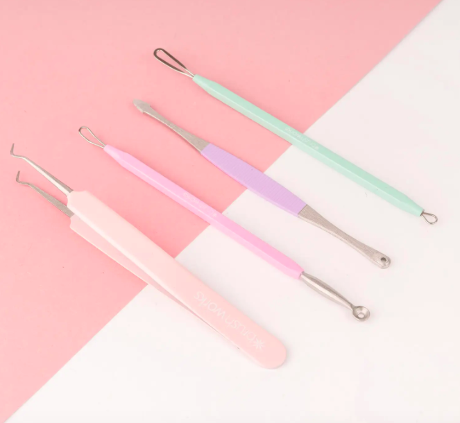 A flatlay of four extraction tools in pastel shades; three are double-ended