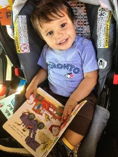 Child in a car seat with his book, about to be strapped in.