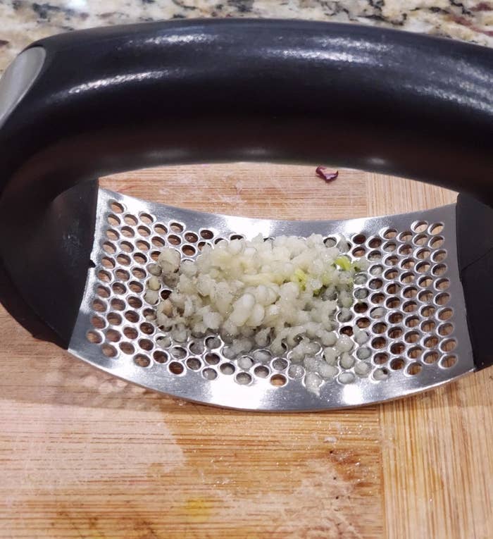 reviewer photo of the rolling handheld garlic press with minced garlic in it