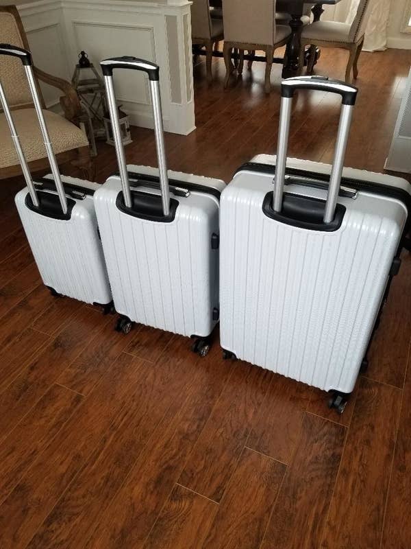 reviewer&#x27;s three white suitcases of different sizes with the handles up