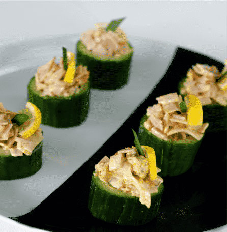 Cucumber segments topped with a blend of cream, ham, tomato and curry powder, with lemon garnishes.