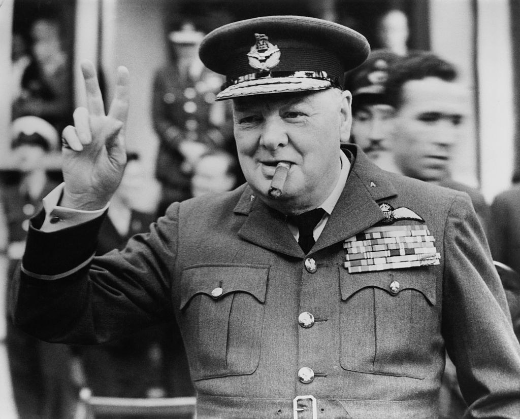 Winston Churchill holding up a V with his fingers and smoking a cigar