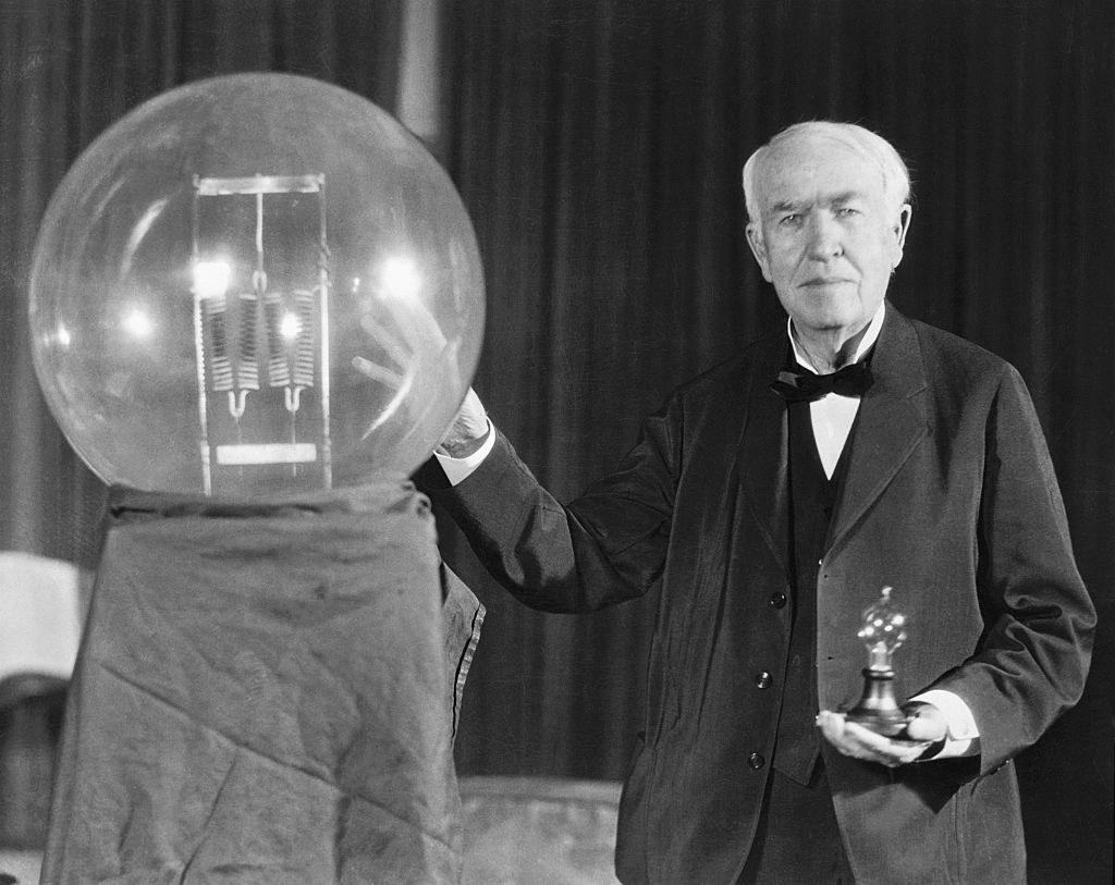 Thomas Edison standing next to his first successful lamp