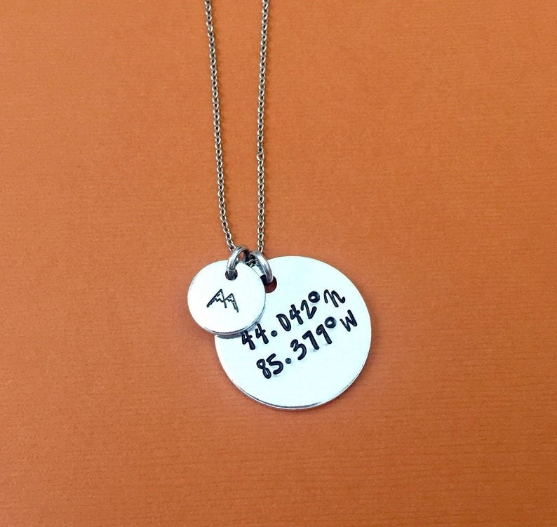 a necklace with coordinates on it and a mountain charm